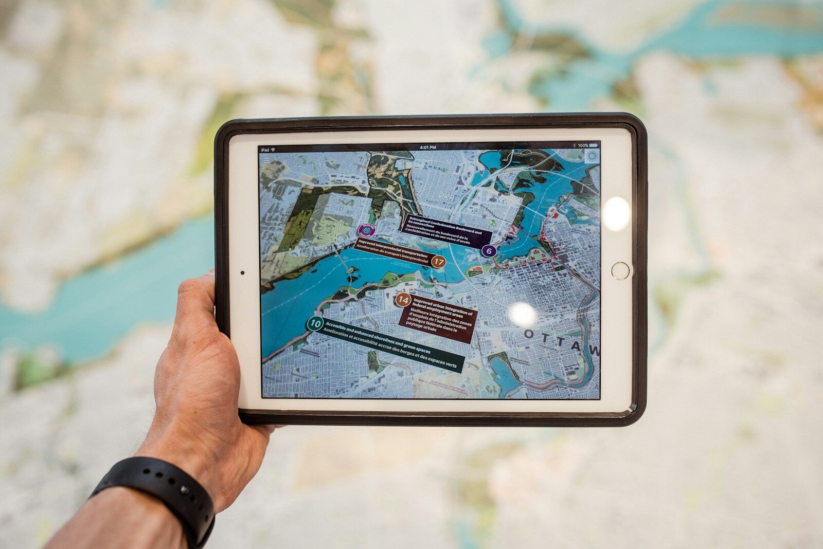 A hand holds a tablet displaying an interactive map of Ottawa, highlighting key features and accessibility information against a blurred background.