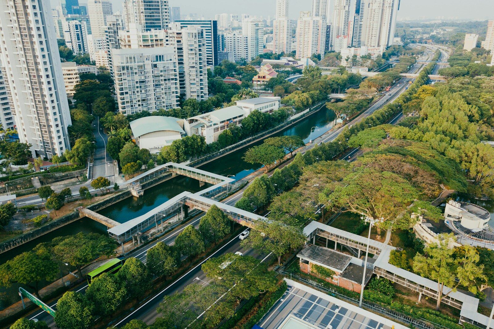 Aerial view of a bustling urban area featuring modern high-rise buildings, a winding canal bordered by green spaces, and roads with traffic.